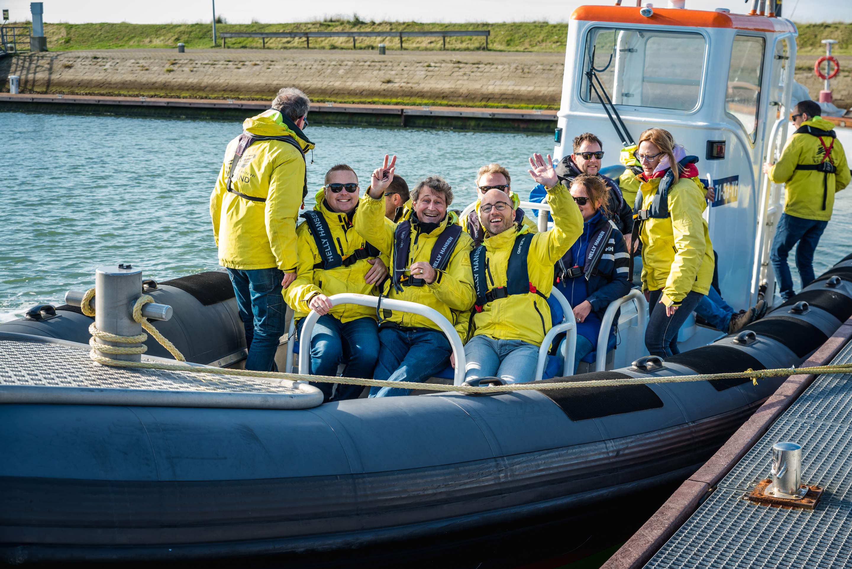 Groep in gele jassen zwaait en lacht vanuit een speedboot in de haven van Vlieland